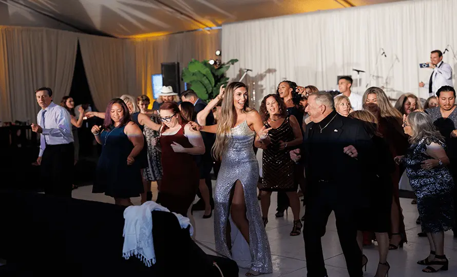 Large group of people dancing at an event with a band performing in the background.