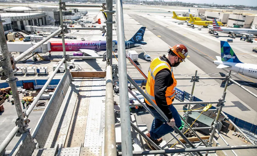 Construction worker on scaffolding at an airport construction site, planes in the background.