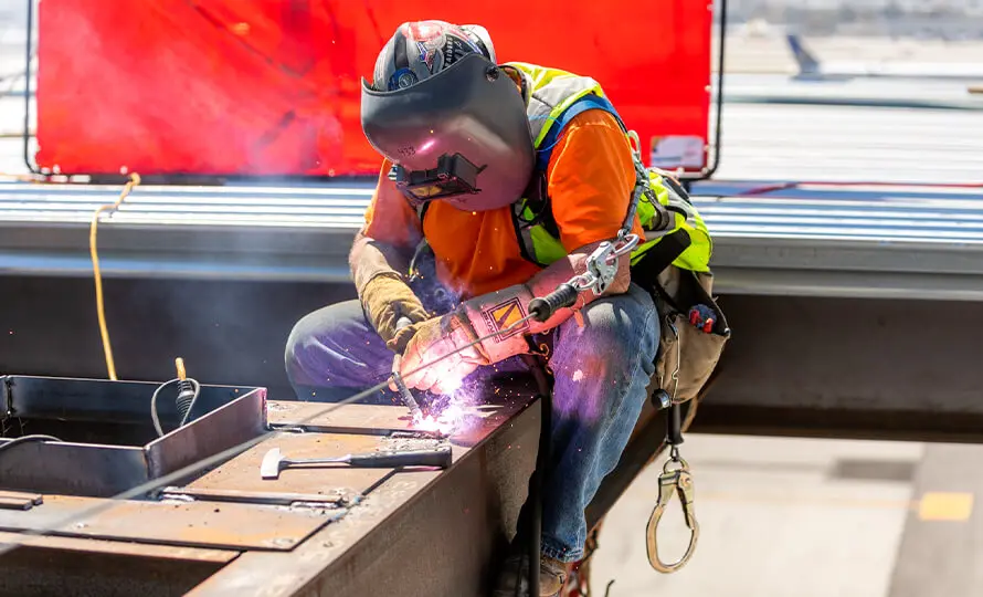 Construction worker welding steel beams, sparks flying, wearing safety gear.