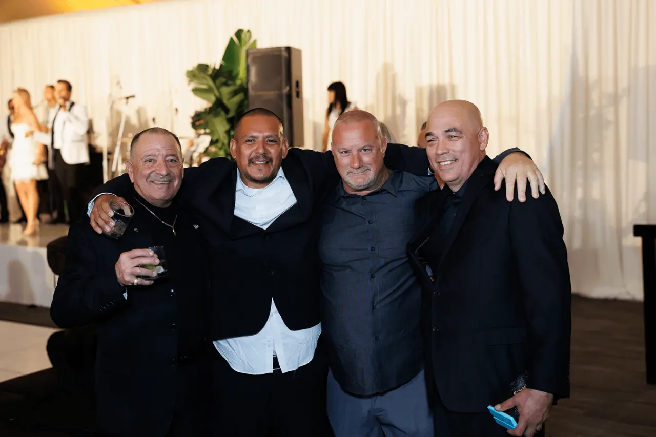 Four men posing for a photo at a formal event with soft lighting.