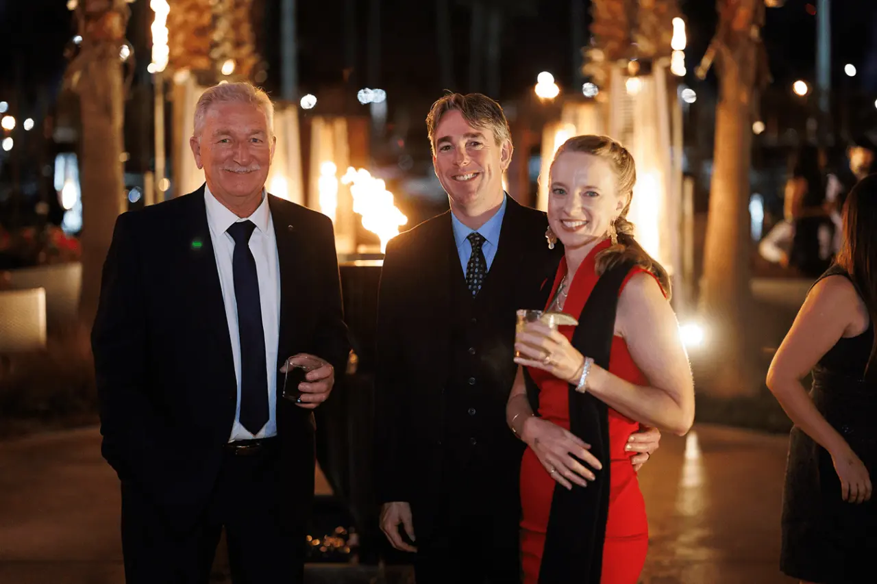 Three people posing for a photo at a nighttime event with fire features in the background.