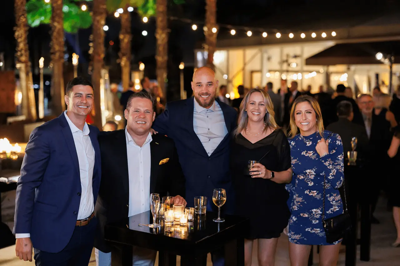 Group of five people posing at a nighttime event with decorative lighting and candles.