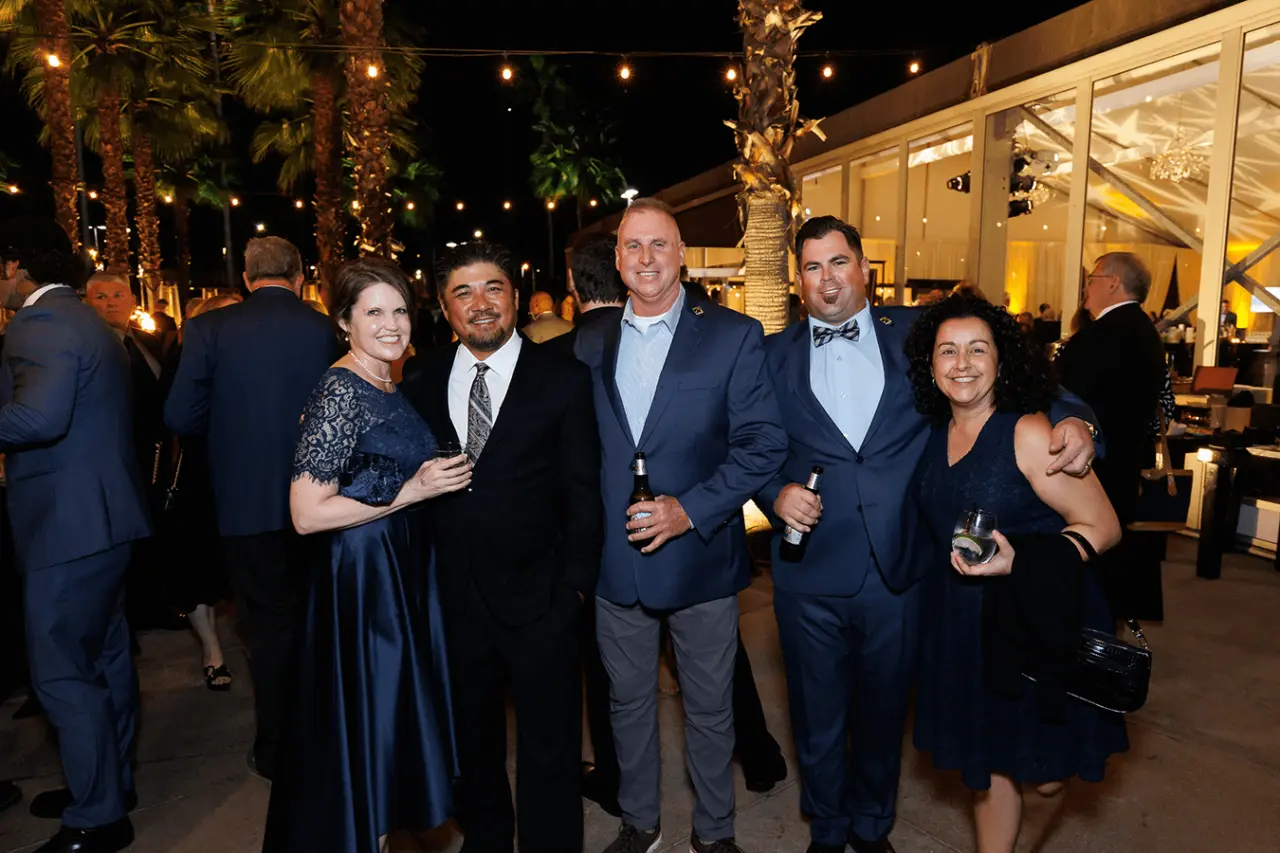 Group of five people posing at an evening event with string lights.