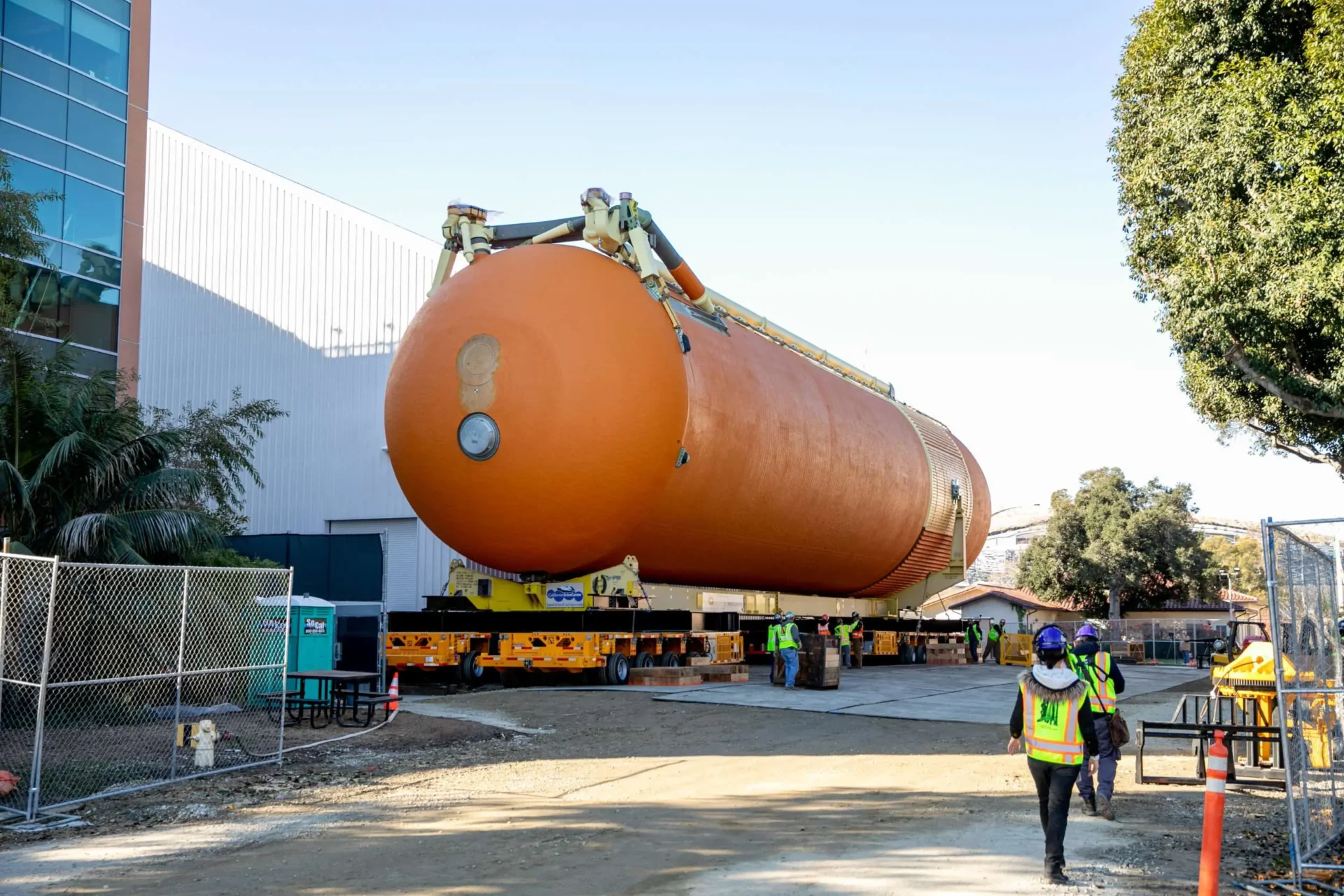 A large orange tank is being carefully loaded onto a truck for transportation.