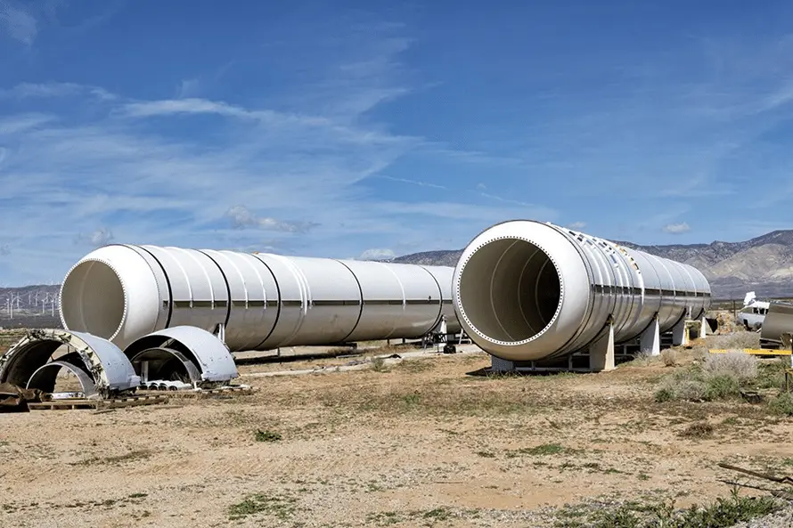 A large pipe stands prominently in the center of a desert field under a clear blue sky.