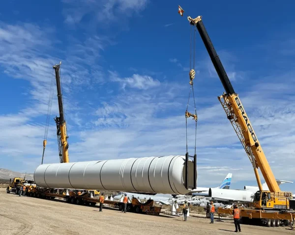 A crane elevates a large white pipe, demonstrating industrial activity at a construction site.