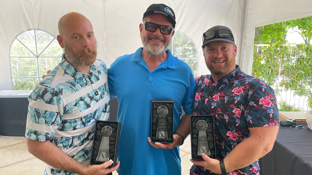 Three men holding trophies after winning a golf tournament.