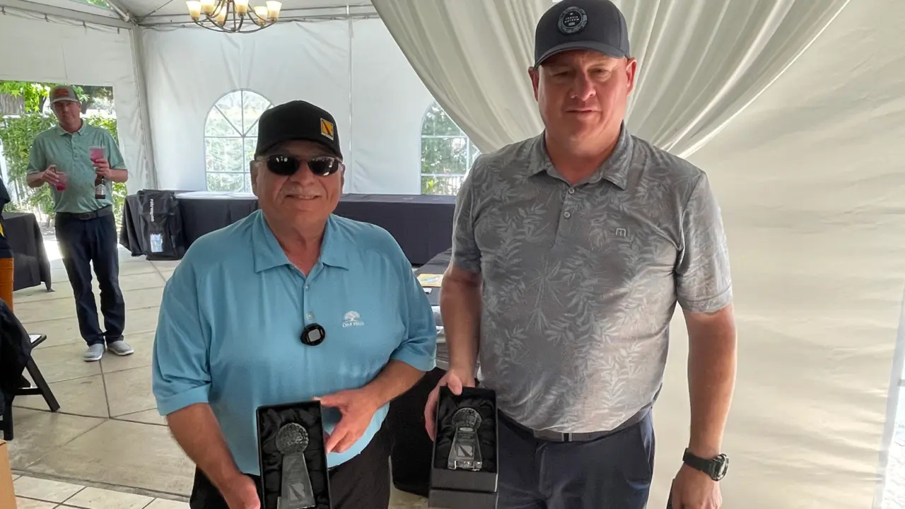 Two men holding trophies after winning a golf tournament.