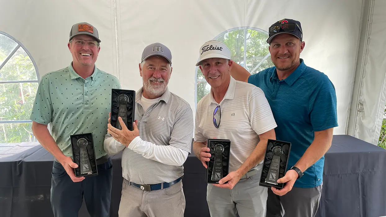Four men holding trophies after winning a golf tournament.