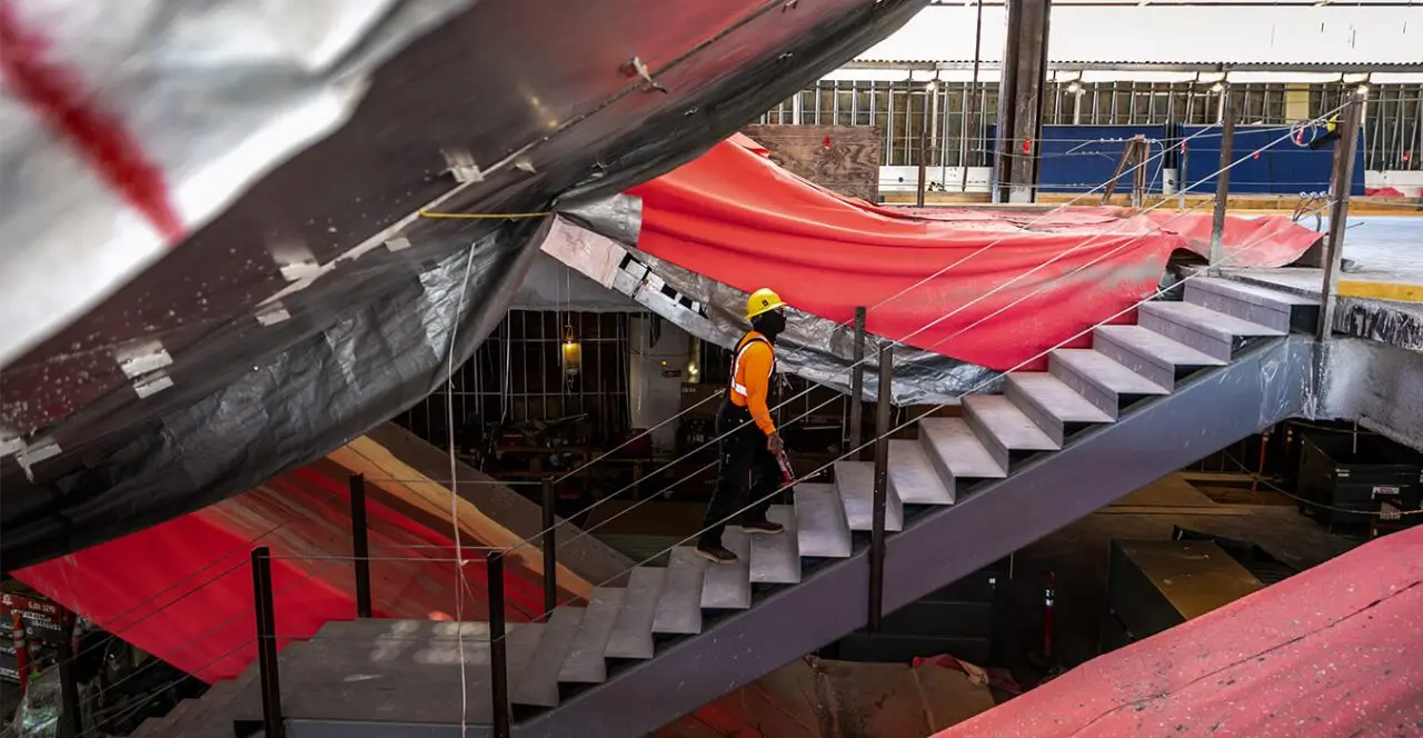 Construction worker descending stairs inside the framework of a bridge or structure.