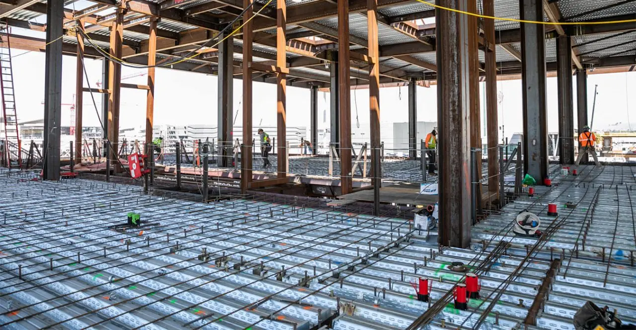 Reinforcing steel (rebar) grid laid out on a bridge deck during construction, with workers present.