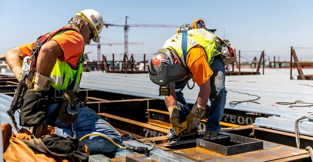 Construction workers welding steel beams on a bridge deck.