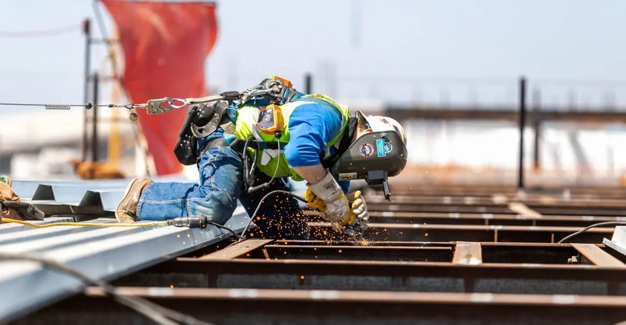 Construction worker welding steel beams on a bridge deck, sparks flying.