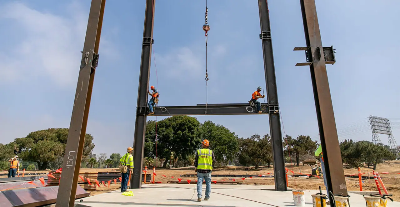 Construction workers securing a steel beam high above the ground on a construction site.