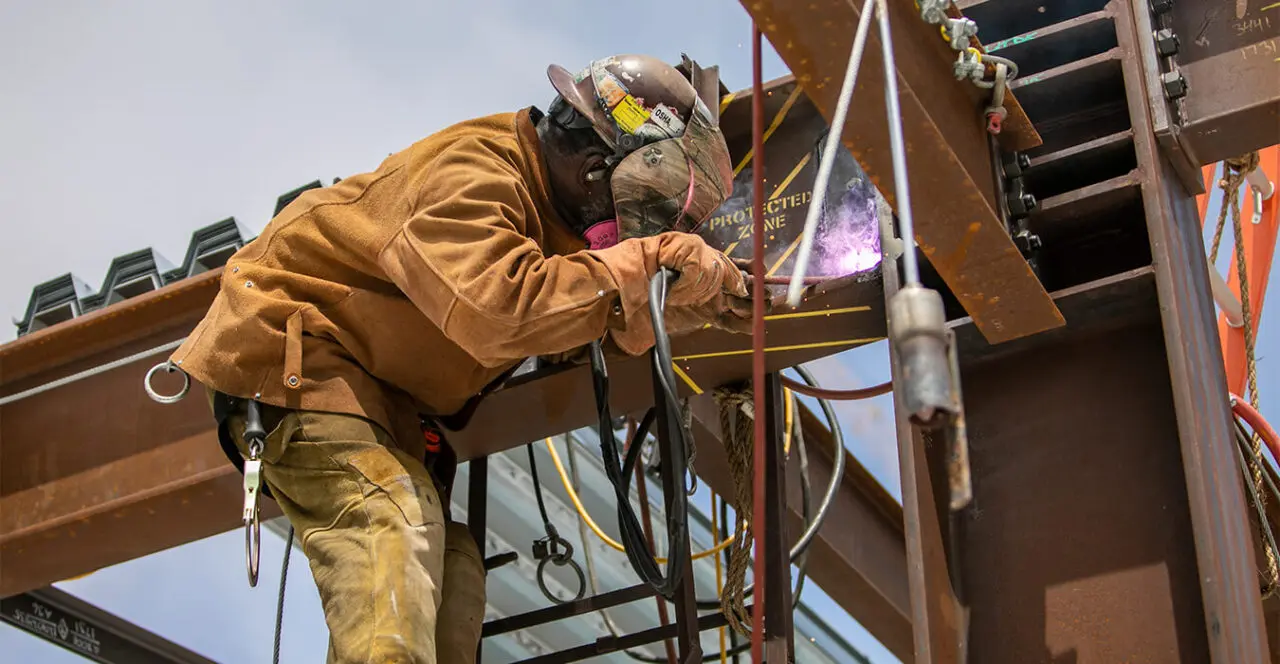 Construction worker welding steel beams high above the ground on a construction site.