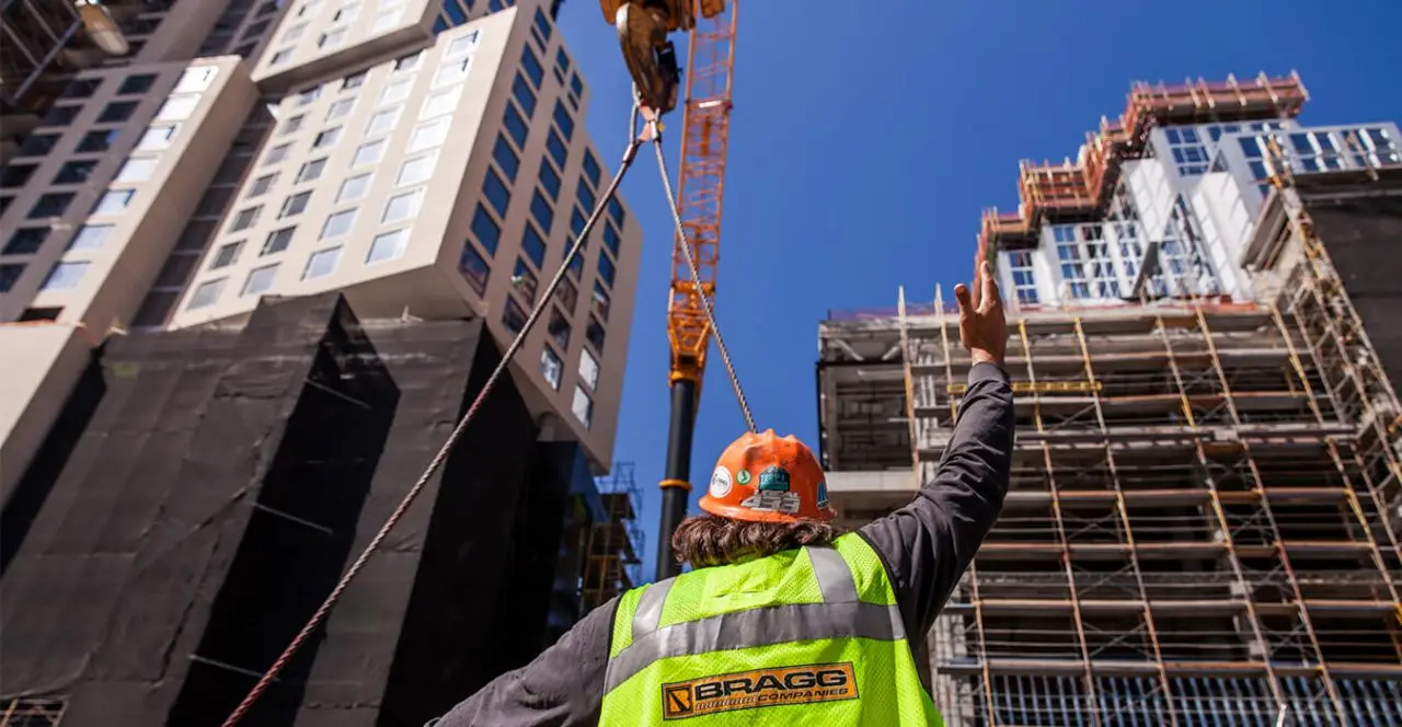Construction worker directing crane operations at a high-rise building site.