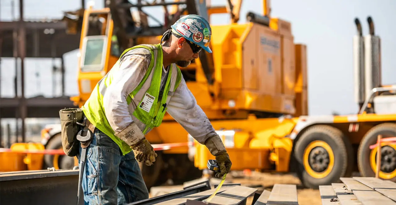 Construction worker measuring steel beams on a construction site.