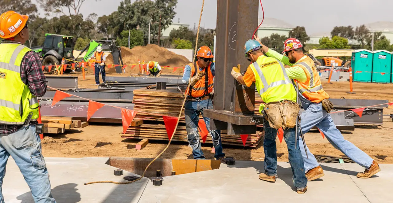 Construction workers aligning and securing a steel beam on a construction site.