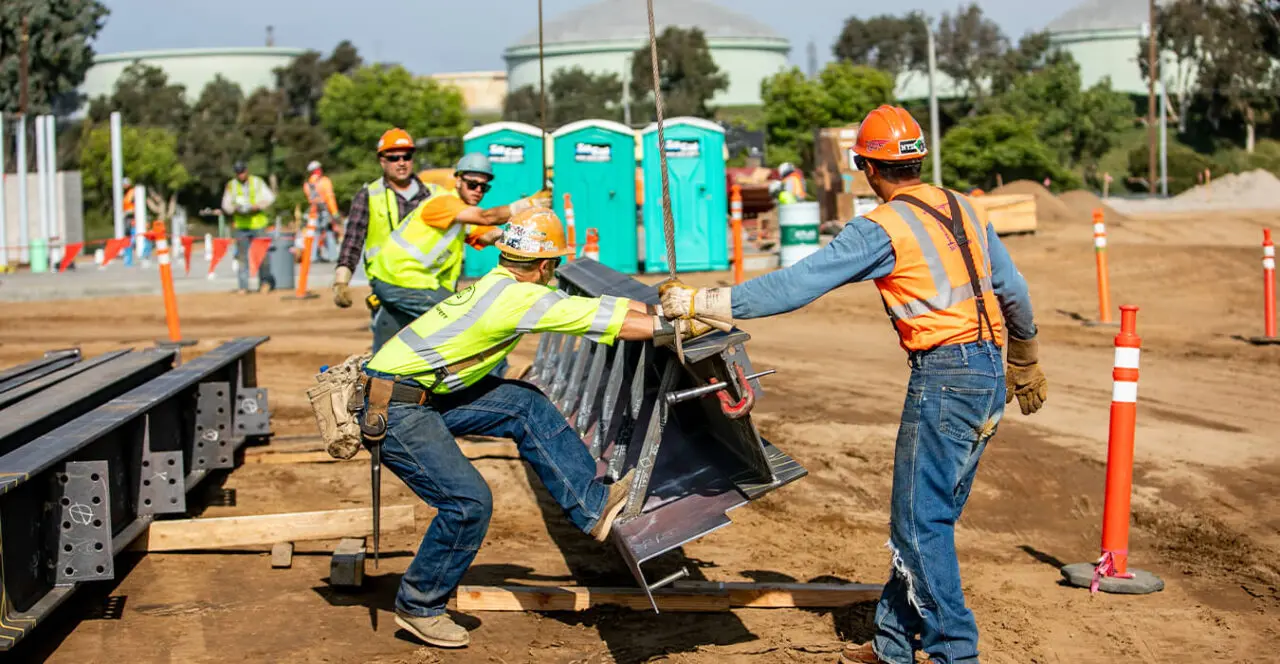 Construction workers lifting and maneuvering steel beams on a construction site.