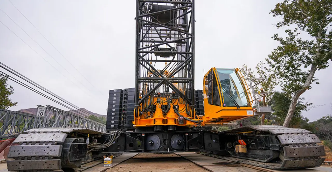 Large orange crane on tracks positioned over a bridge during construction.