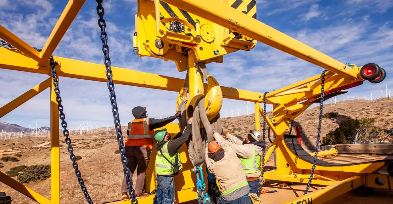 Workers connecting a load to a crane hook at a wind farm site.