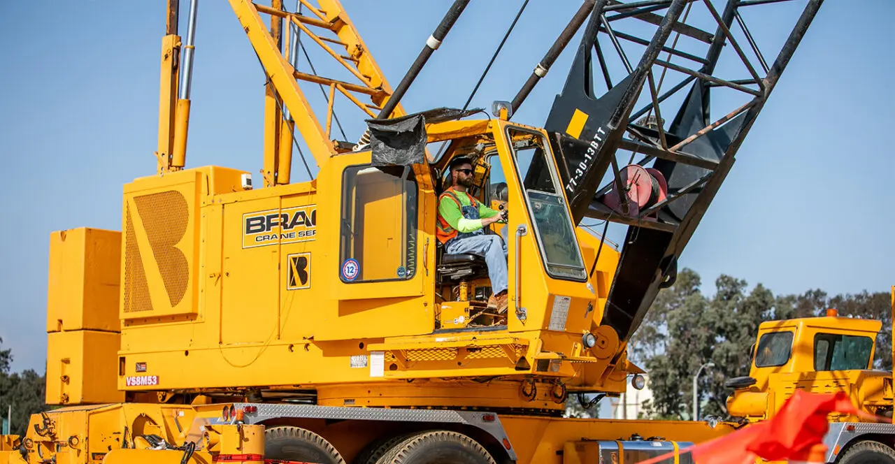 Crane operator in the cab of a large yellow crane.