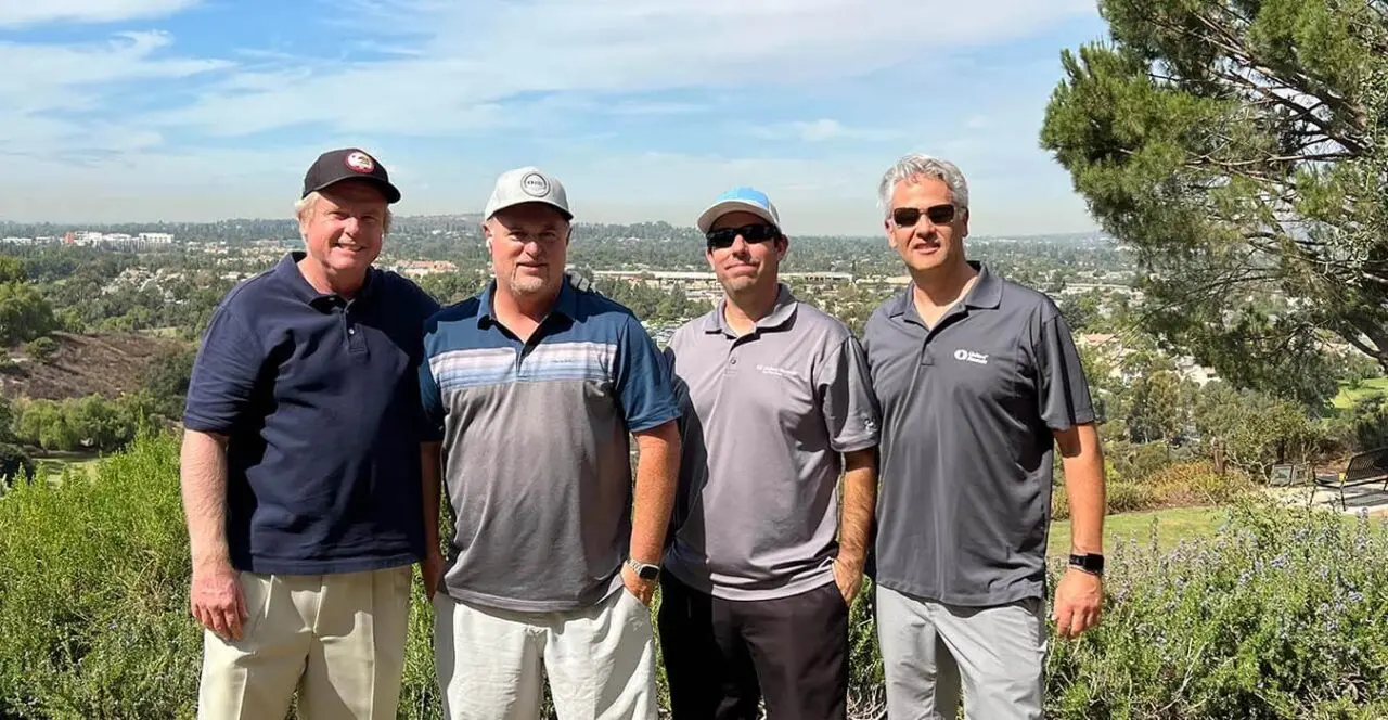 Four men posing on a golf course overlooking a city skyline.