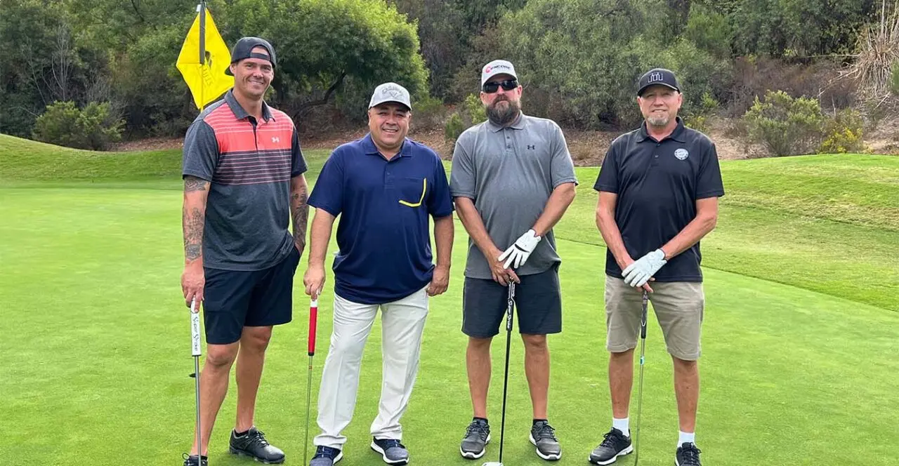 Four golfers posing on a golf course during a sponsored event.