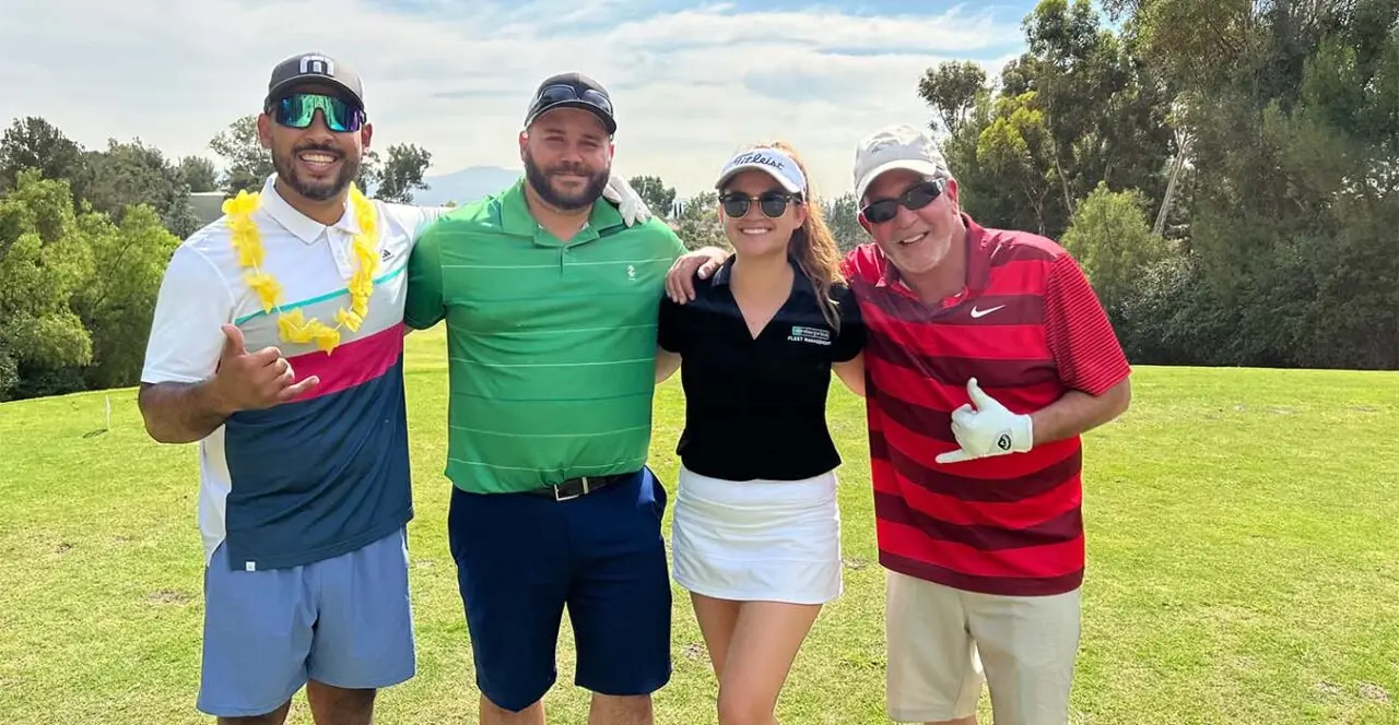 Four golfers posing on a golf course, with one wearing a lei.