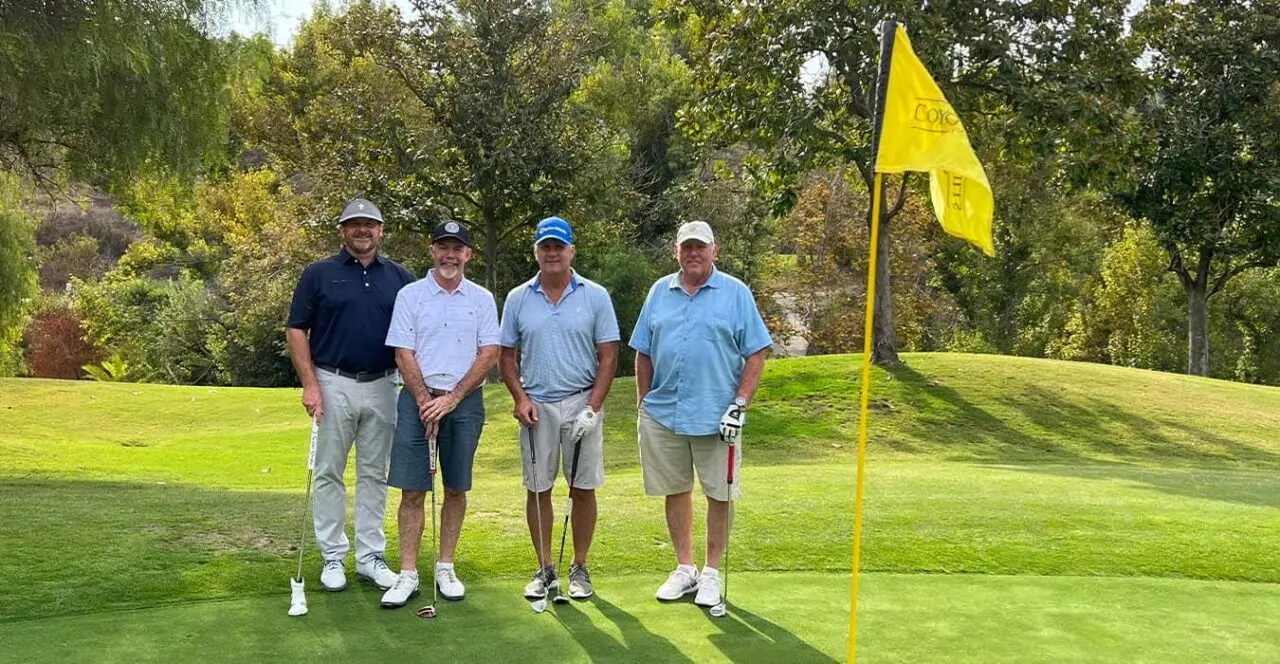Four golfers on a golf course green near the pin.
