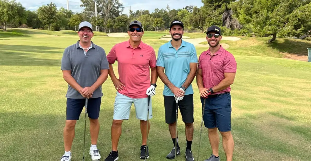 Four golfers posing on a green golf course during a sponsored event.