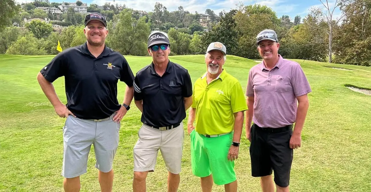 Four golfers posing on a green golf course during a tournament or event.