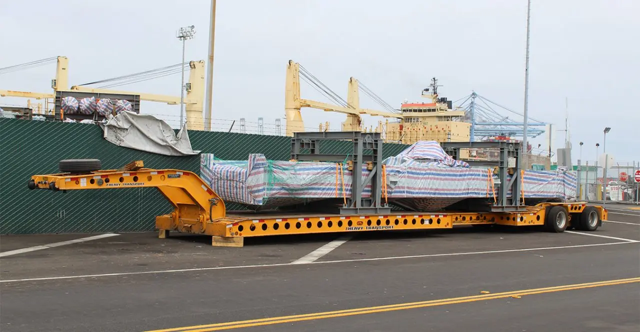 Large covered components transported on a heavy-duty trailer at a port or industrial facility.