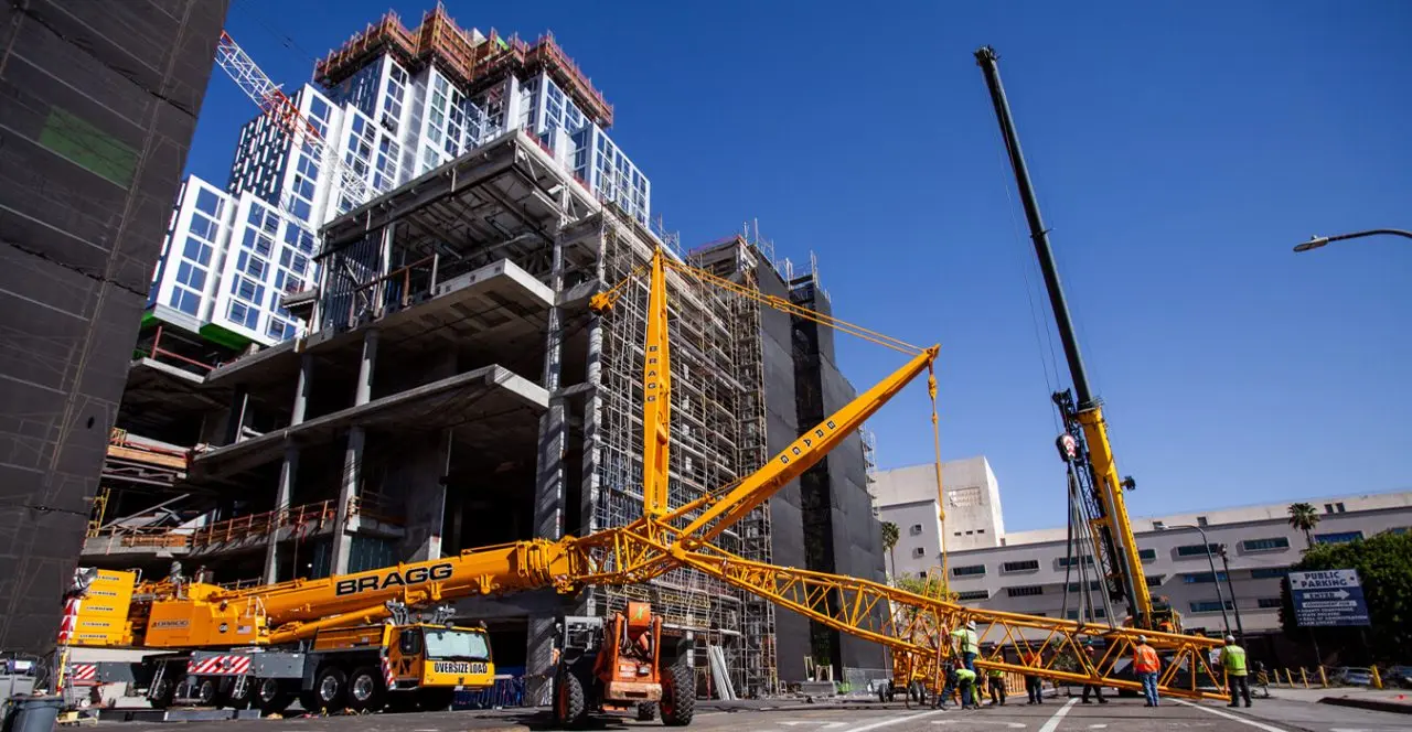 High-rise building under construction with a large crane lifting materials on a city street.