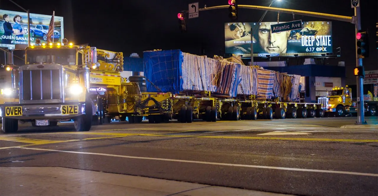 Oversize load being transported through a city at night, with a warning sign on the trailer.