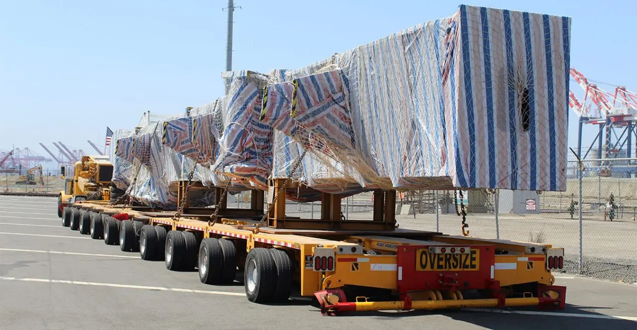 Oversize load being transported on a multi-wheeled trailer near a port, with “oversize” clearly visible on the trailer.