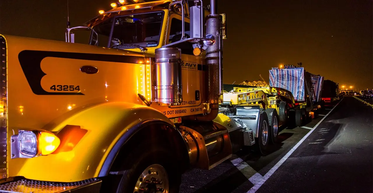 Close-up of a large yellow semi-truck with bright lights at night, part of an over-sized load transport.