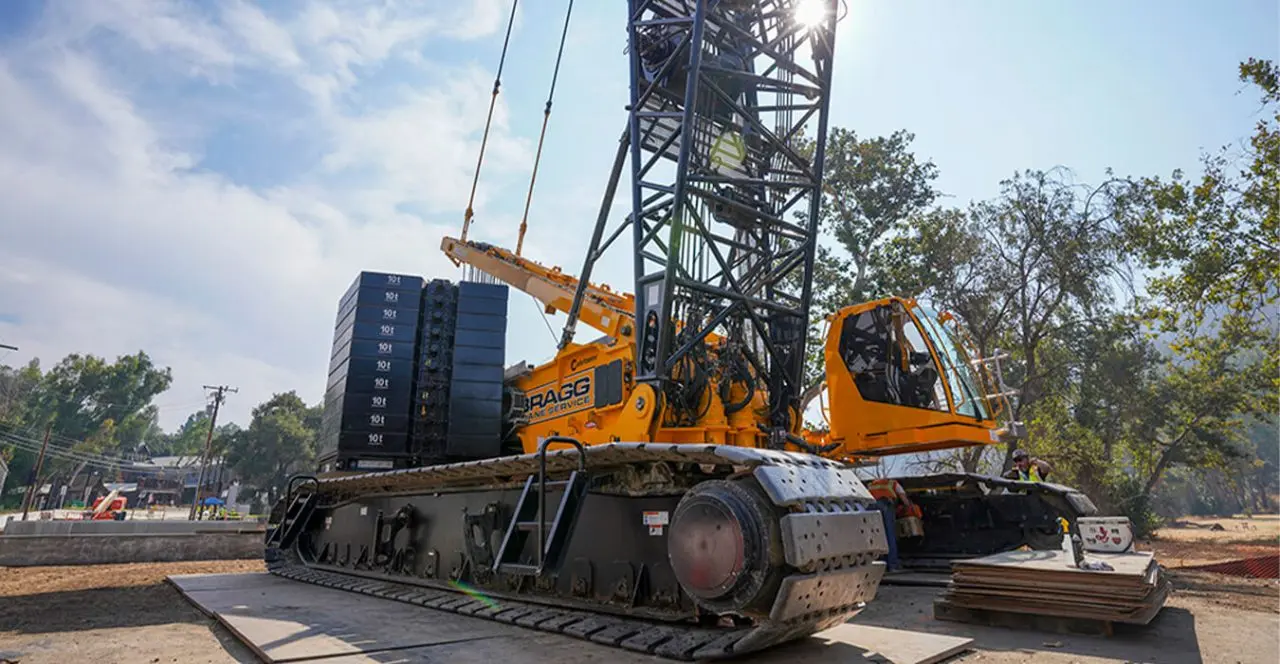 Large crane lifting a stack of solar panels at a construction site.
