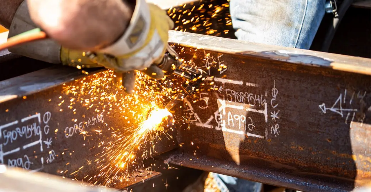 Construction worker welding or cutting steel beams, with sparks flying.