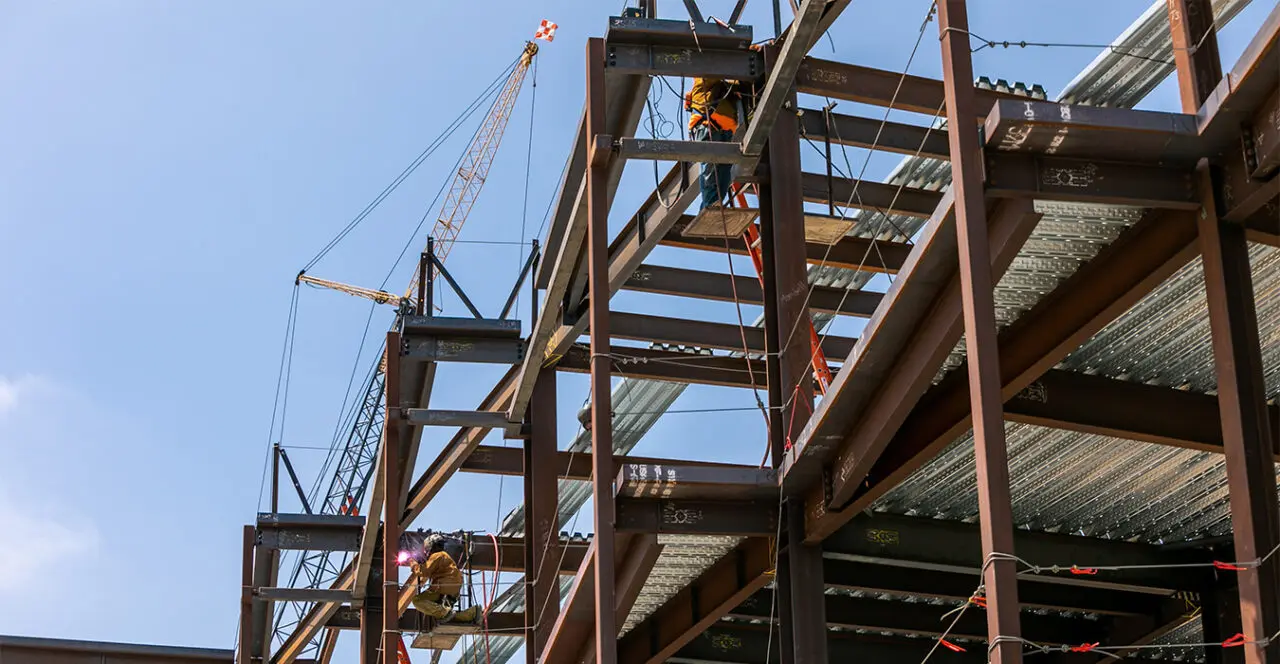 Construction workers welding steel beams high up on a building’s frame.