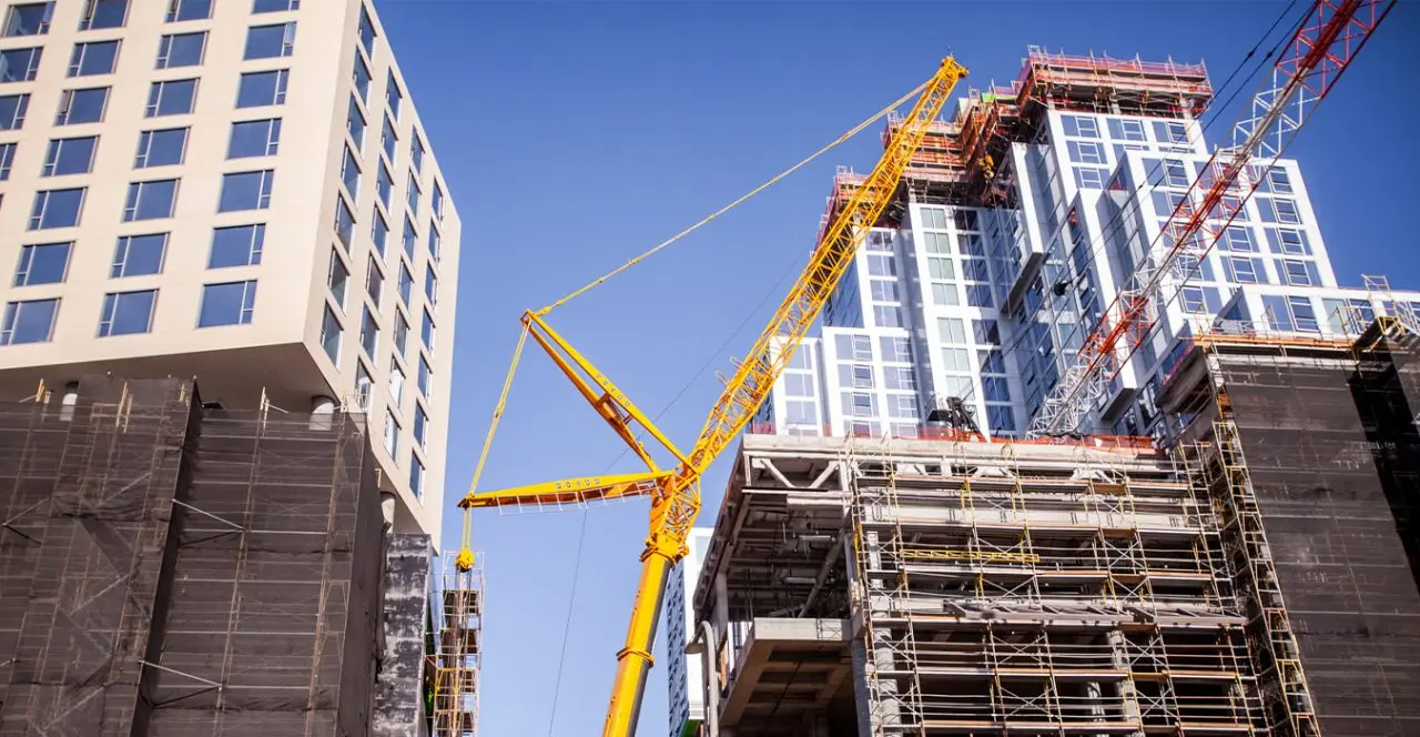 Tall construction crane lifting materials between high-rise buildings under construction.
