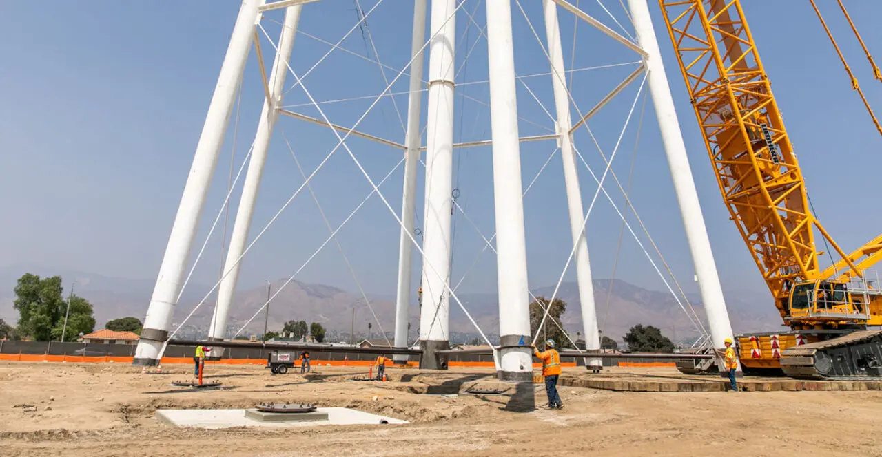 Construction workers surrounding the base of a rising water tower.