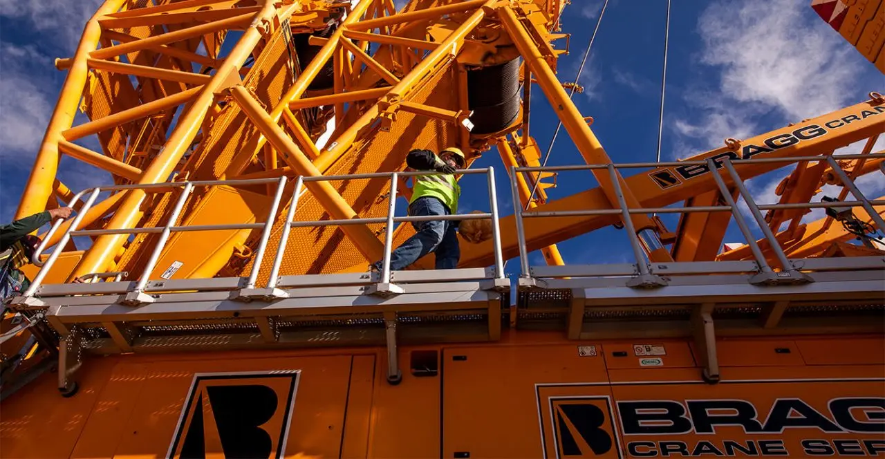 Crane technician inspecting wind turbine crane boom at renewable energy site.