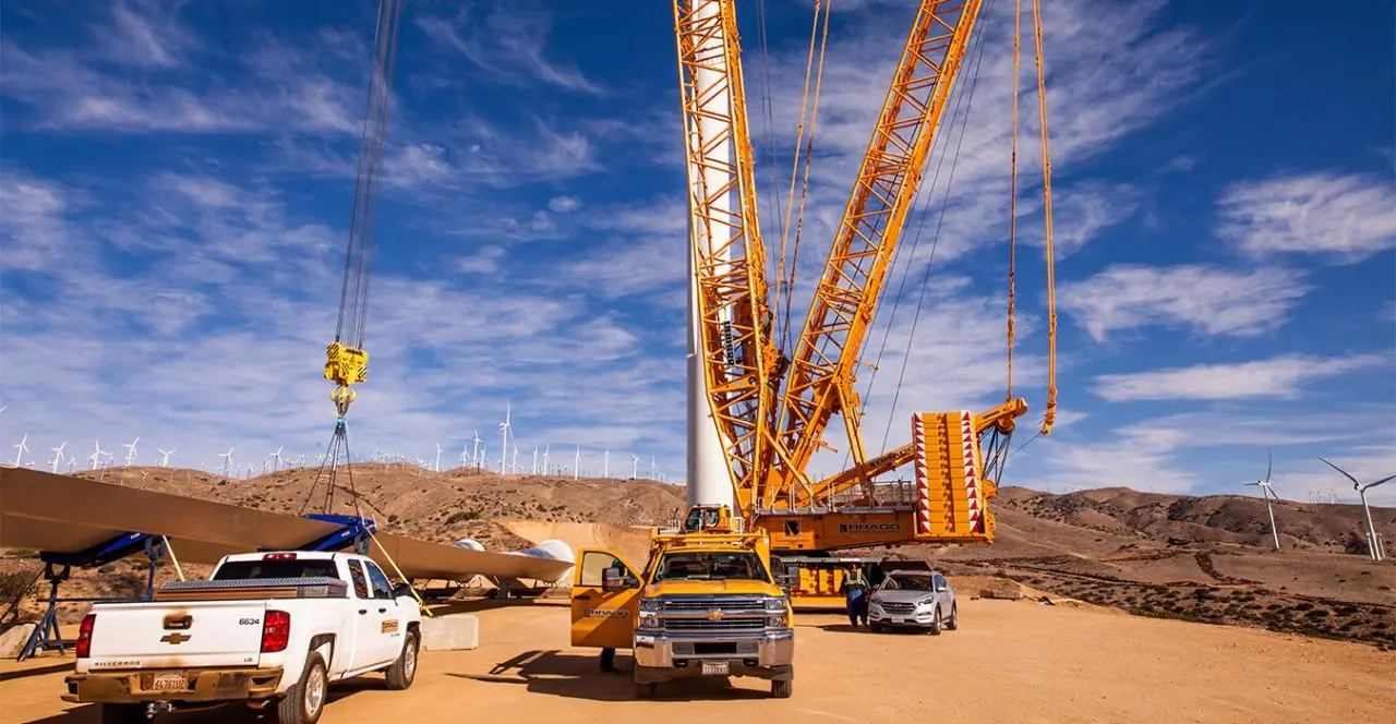 Large crane lifting a wind turbine tower section at a renewable energy farm.